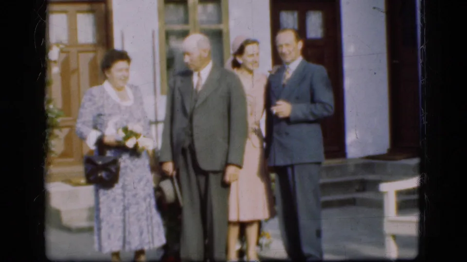 1975 Denmark frame of a formal group outside a building entrance, with flowers, dresses, suits, and visible 8mm softness.