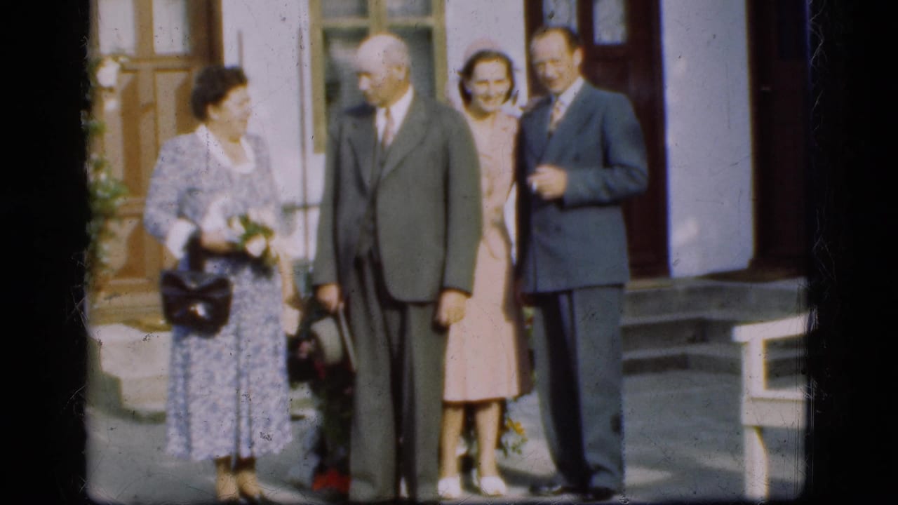 In Denmark archival 8mm footage, four adults in formal 1970s clothing stand by a building entrance, including a woman with a bouquet.