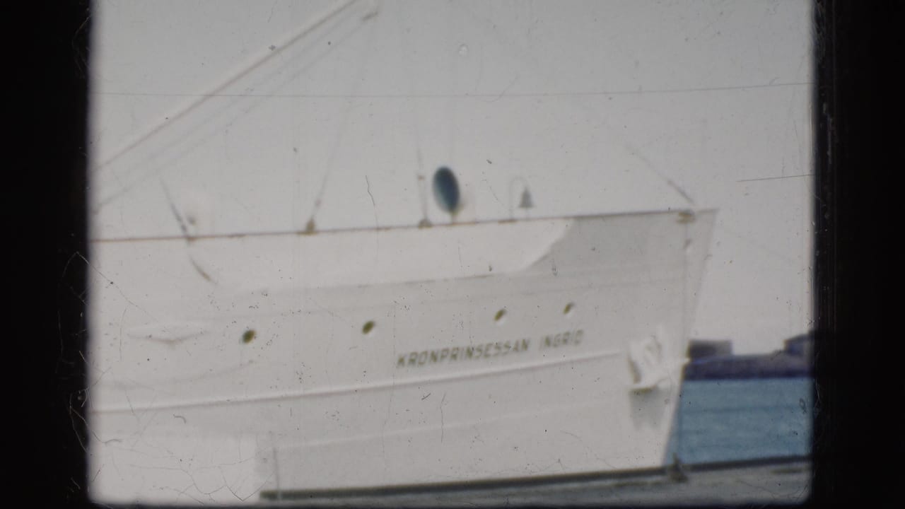 1975 Denmark 8mm frame showing the white hull of Kronprinsessan Ingrid docked at harbor with portholes and rigging visible.