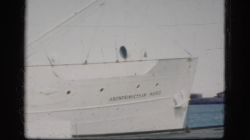 1975 Denmark 8mm frame showing the white hull of Kronprinsessan Ingrid docked at harbor with portholes and rigging visible.