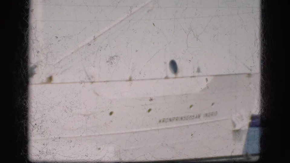 Soft 8mm view of the docked Kronprinsessan Ingrid hull in Denmark, with partial name lettering, portholes, and harbor water.
