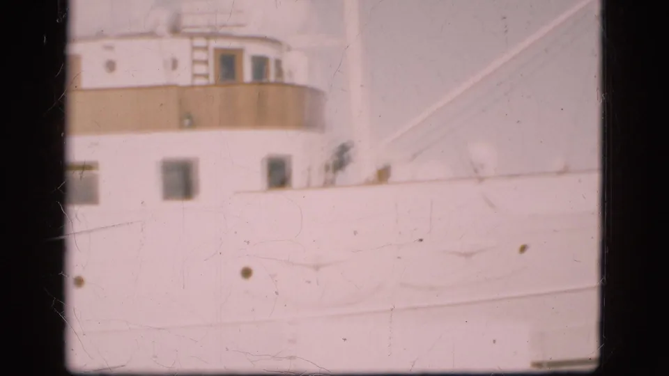 Faded 8mm frame of Kronprinsessan Ingrid in a Danish harbor, emphasizing the cream upper deck, windows, and white hull.