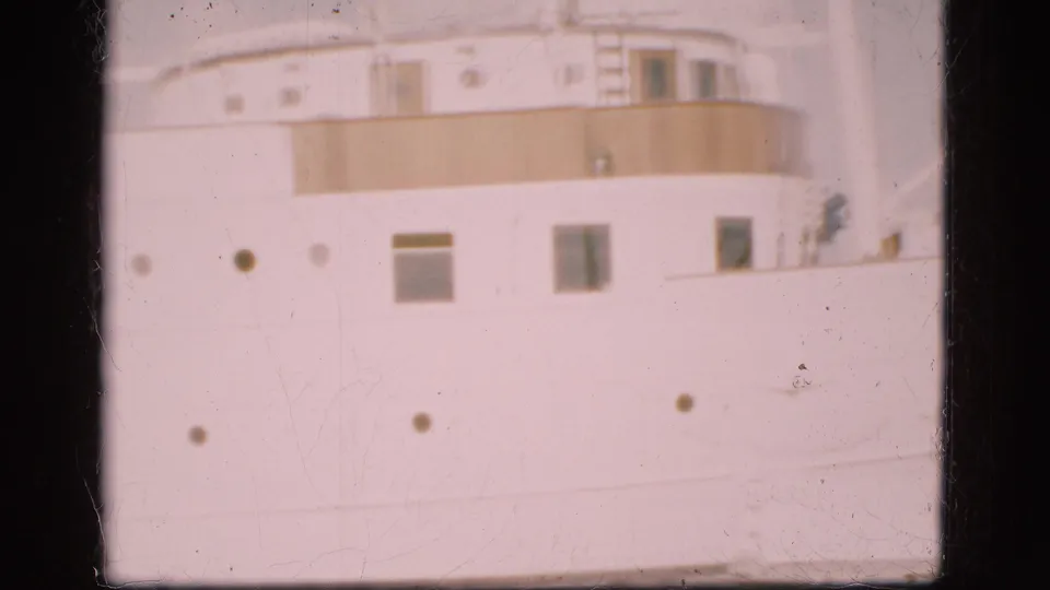 1975 Denmark 8mm frame of a white passenger ship exterior, showing portholes, windows and a tan upper deck band.