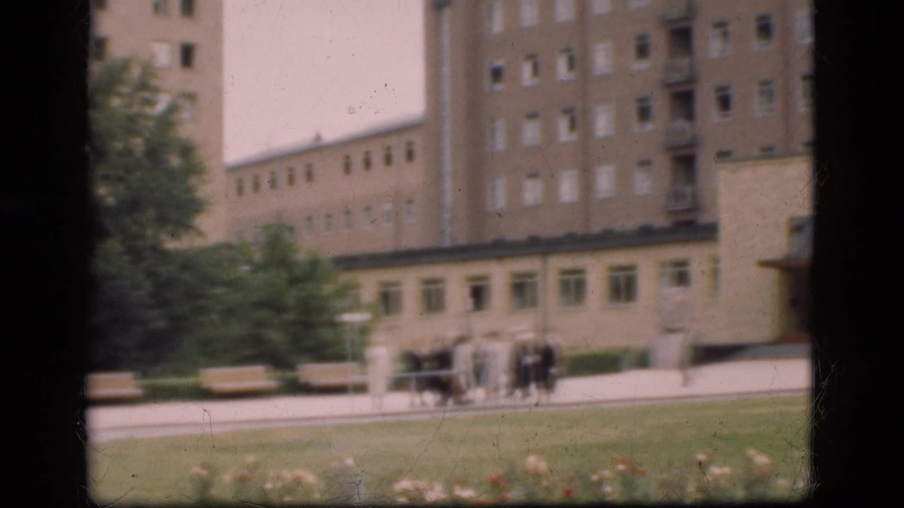 In Denmark in 1975, a small group of people walks near benches and lawn in front of a large modernist institutional-looking building.