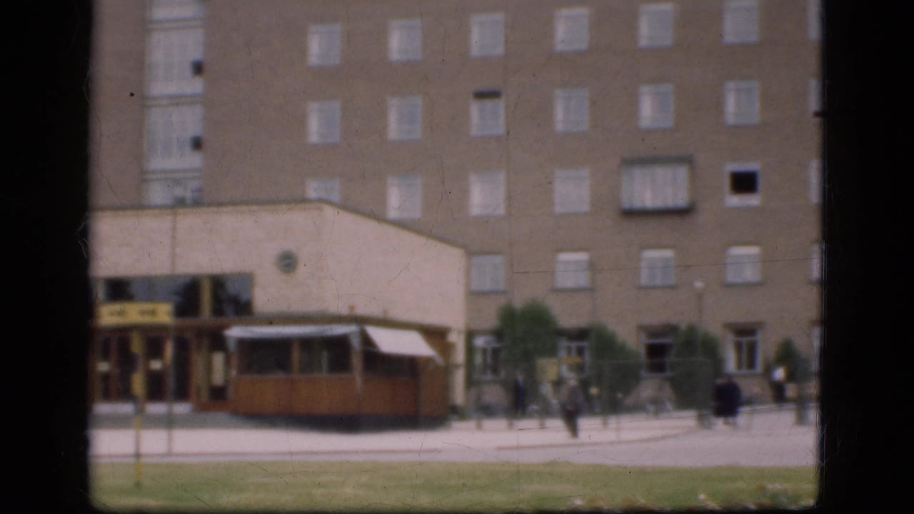 Street frontage with brick building, kiosk, pedestrians, and open pavement.