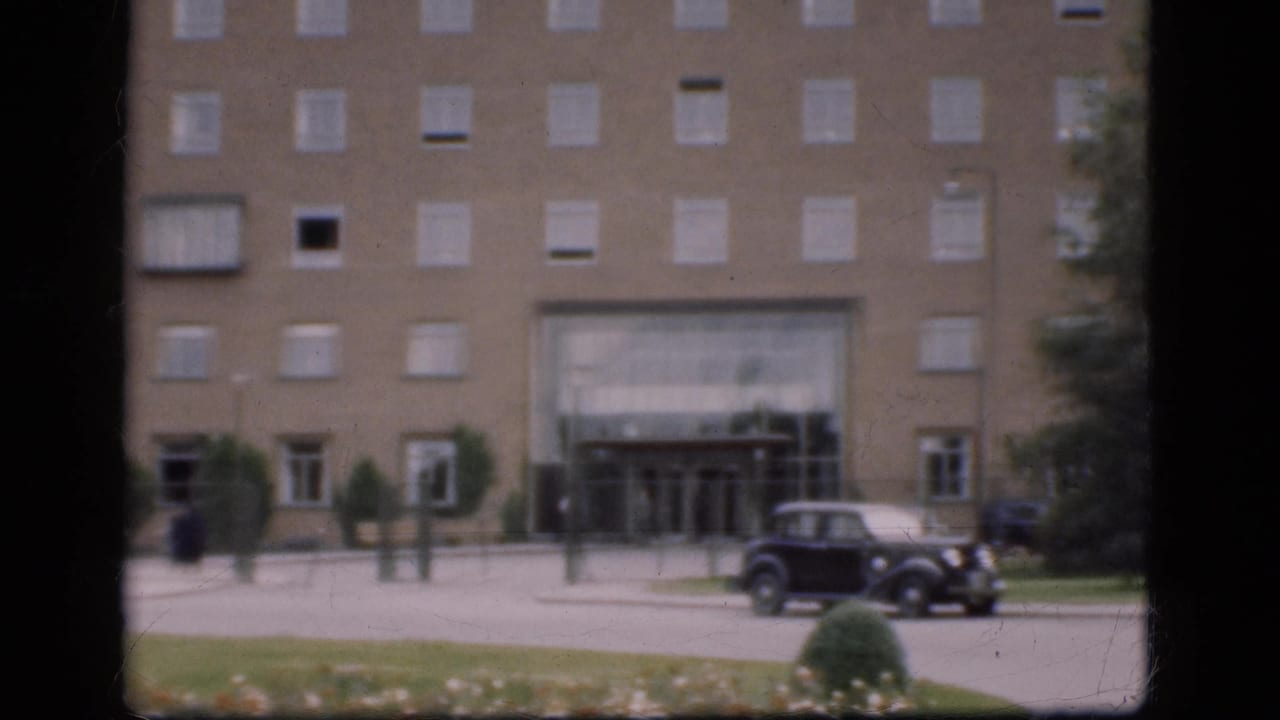 Large building with parked dark car, lawn, shrubs, and window-frame borders.