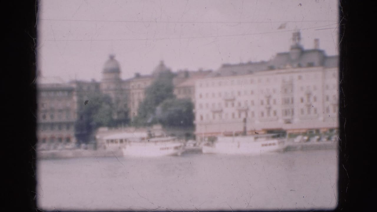 1975 Denmark 8mm frame showing a hazy riverside cityscape with pale buildings, trees, boats, and a domed roof in the background.
