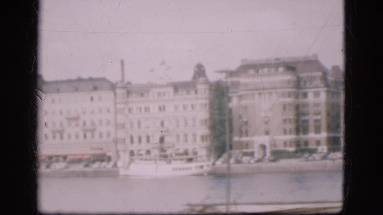 1975 Denmark frame with large waterfront facades and a white boat near the shore, captured in faded 8mm color.