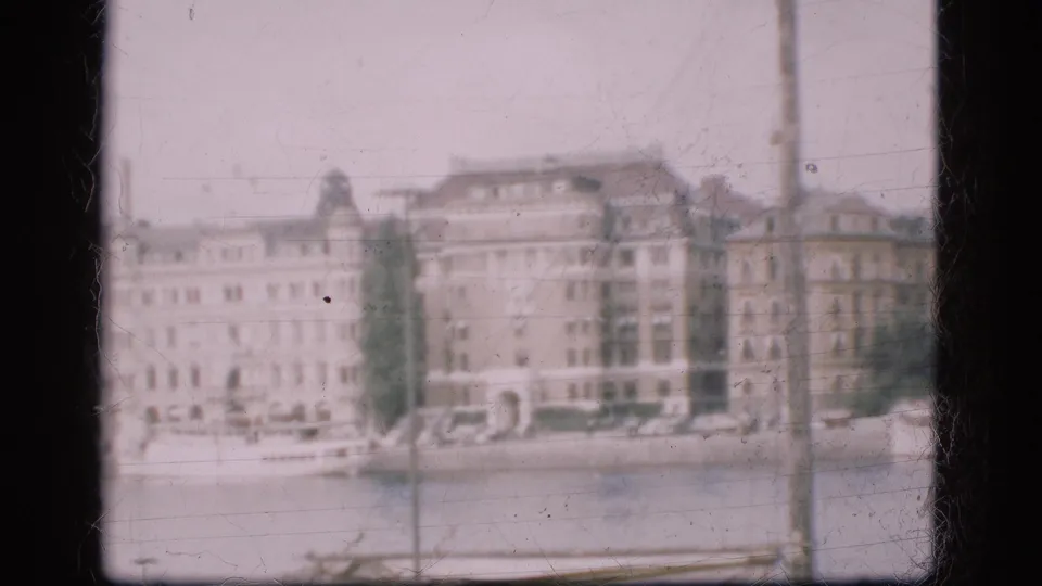 1975 Denmark home-movie frame showing waterfront facades, foreground poles, and calm water during a slow pan.