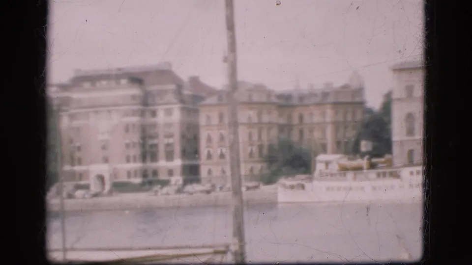 1975 Denmark frame showing large buildings along the water and a boat at the shoreline near the right side.