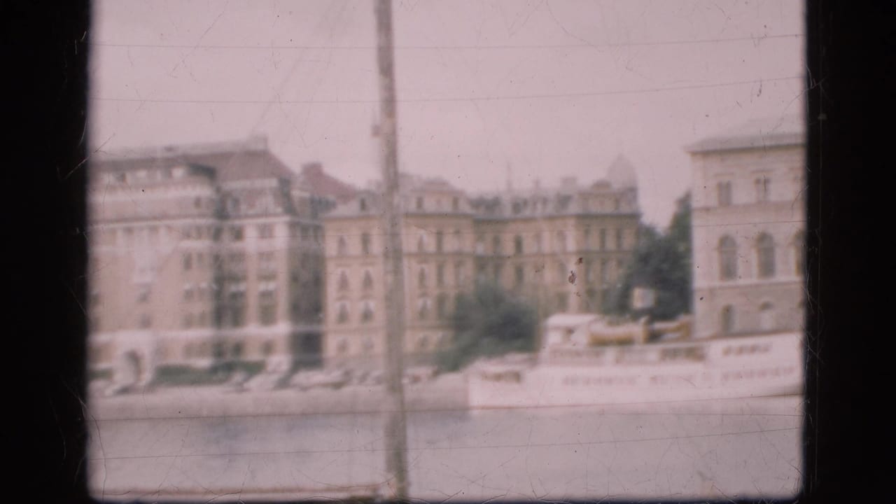 1975 Denmark waterfront view with pale European facades, a moored white passenger boat, trees, quay, and soft 8mm framing.