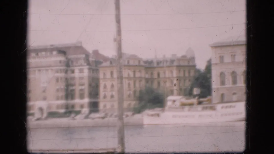 1975 Denmark waterfront view with pale European facades, a moored white passenger boat, trees, quay, and soft 8mm framing.