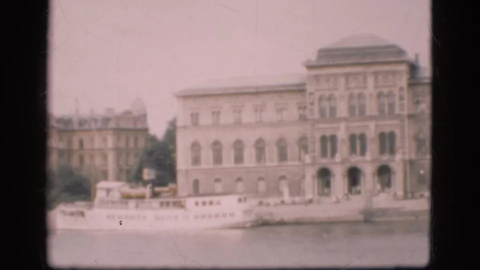 1975 Denmark waterfront frame showing ornate building fronts, arched windows, a partial white boat, and the river edge.