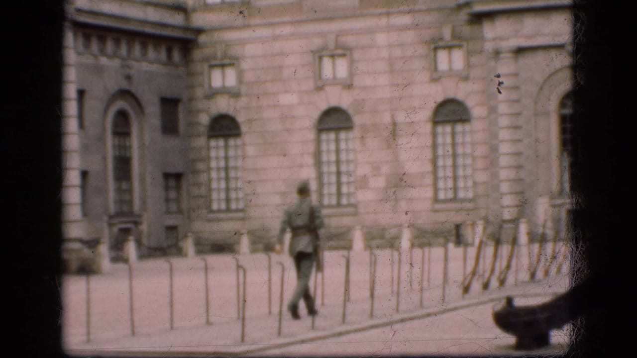 1975 Denmark 8mm frame showing a soldier walking near arched windows and bollards outside a grand stone building.