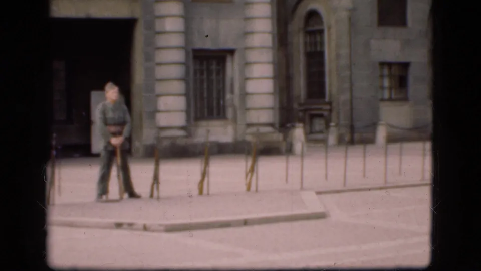 1975 Denmark 8mm frame with a soldier standing near a dark doorway and stone columns in a formal courtyard.