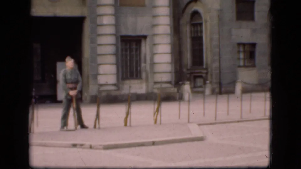 1975 Denmark 8mm frame showing a soldier paused beside a formal stone building and lines of metal bollards.