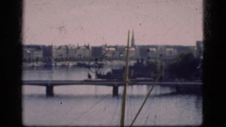 1975 Denmark 8mm frame looking over water toward a bridge, low city buildings, and distant spires.