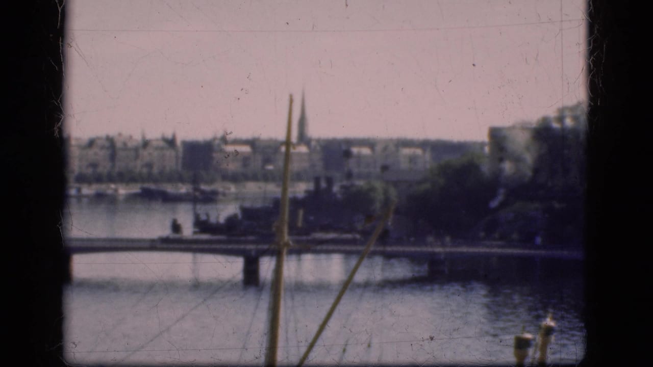 1975 Denmark 8mm frame with a bridge over water, distant buildings, trees, and a church spire behind dark film edges.