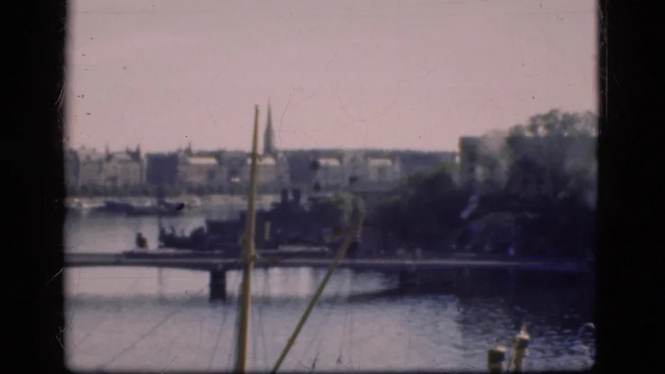 1975 Denmark waterfront frame showing a bridge, mast lines, trees, water, and distant buildings with soft home-movie texture.