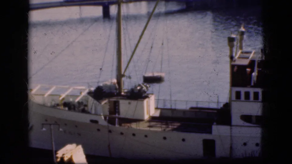 1975 Denmark 8mm frame showing a white moored boat with mast and rigging, with bridge and water in the background.