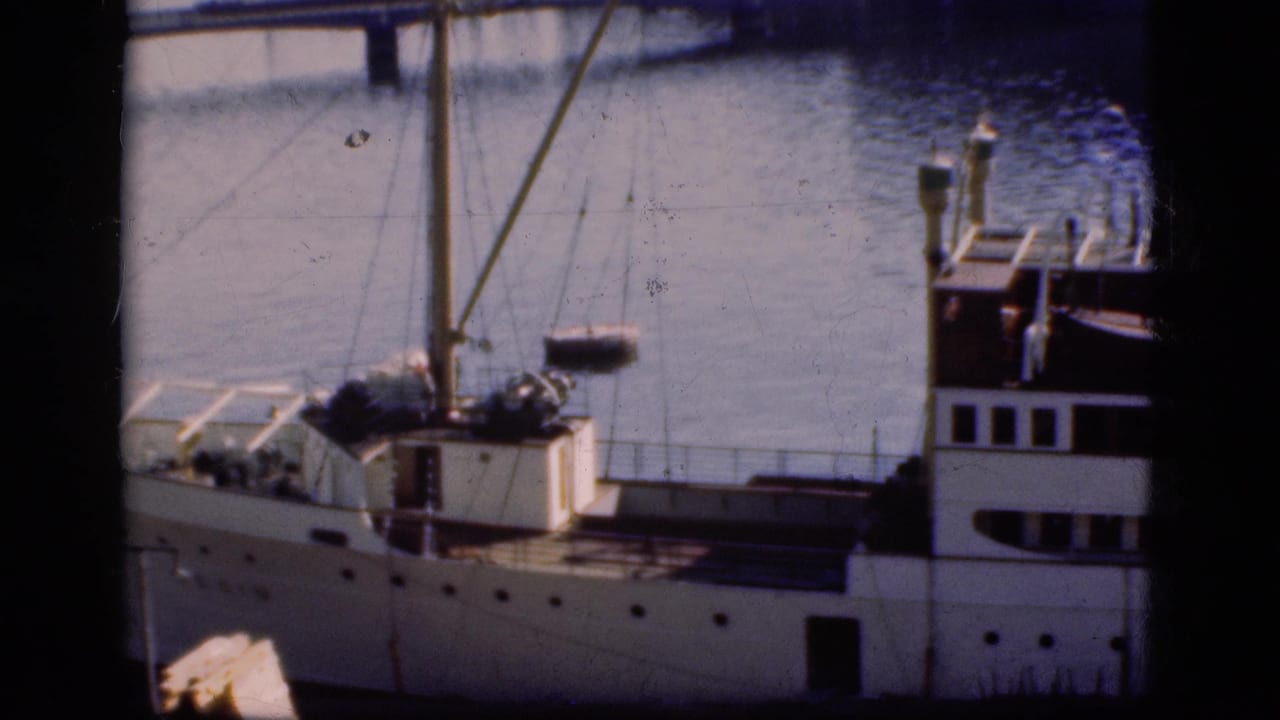 1975 Denmark home-movie frame showing a white docked passenger ship, mast rigging, railings, and calm harbor water.