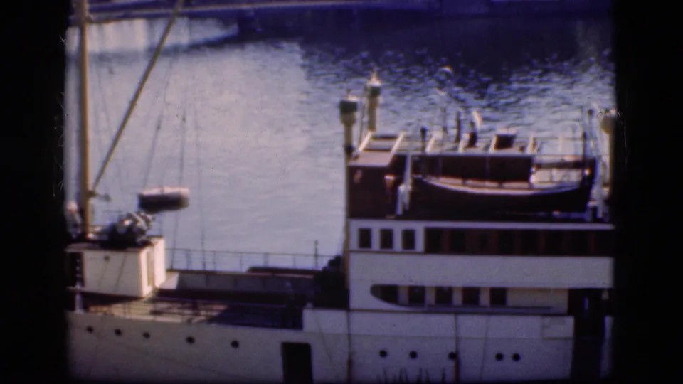 1975 Denmark 8mm frame showing the ship's deck, railings, cabin windows, mast, and blue harbor water.
