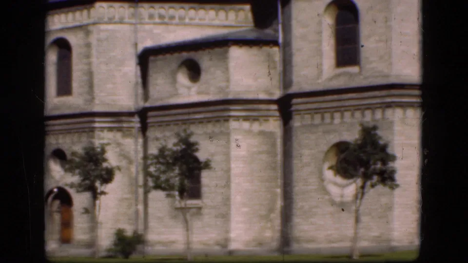 1975 Denmark 8mm frame showing part of a historic pale stone building with arched openings, trees, and lawn.