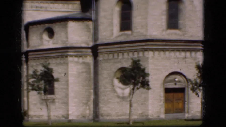 1975 Denmark 8mm frame of a historic stone exterior with a wooden door, arched windows, and small trees.