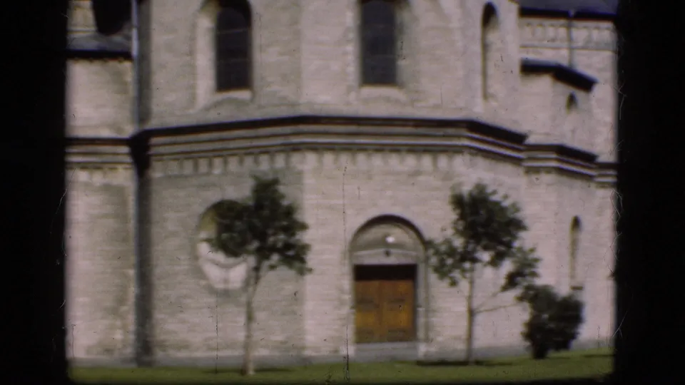 1975 Denmark 8mm frame showing the lower facade of a historic stone building with door, window, trees, and grass.