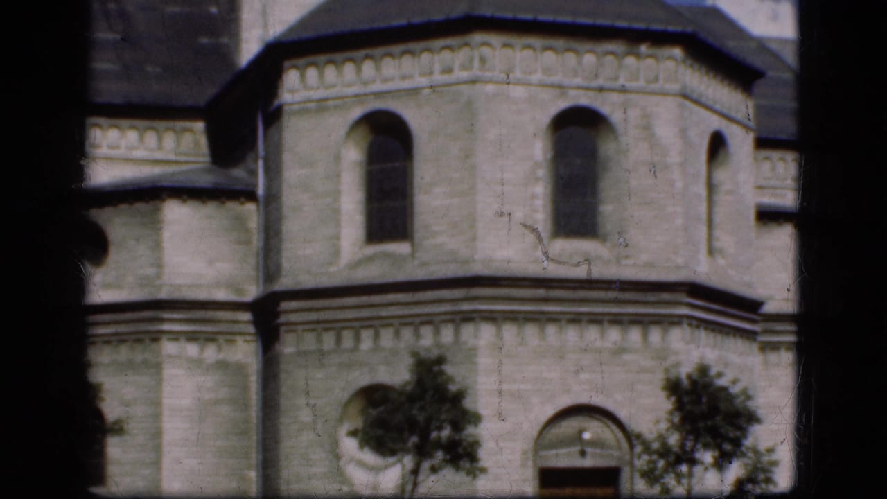 1975 Denmark 8mm frame showing a pale stone church exterior through dark window bars, with arched windows and small trees below.