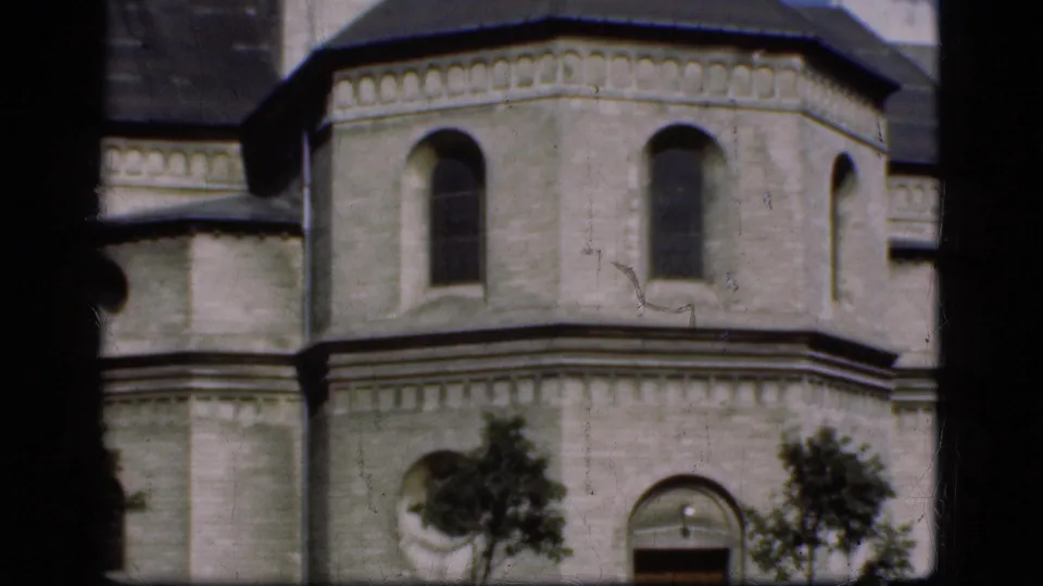 1975 Denmark 8mm frame showing a pale stone church exterior through dark window bars, with arched windows and small trees below.