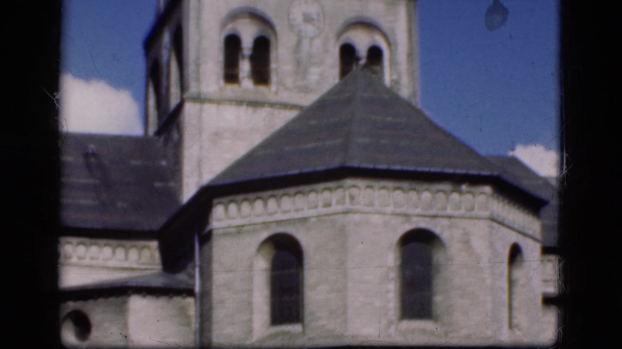 1975 Denmark 8mm frame with the church tower, rounded stone exterior, arched windows, dark roof, and blue sky visible through window framing.