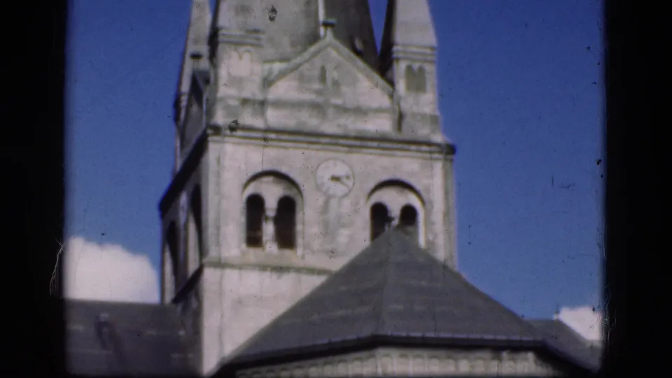 1975 Denmark 8mm frame showing a church tower with arched openings, a clock face, roof sections, and bright blue sky.