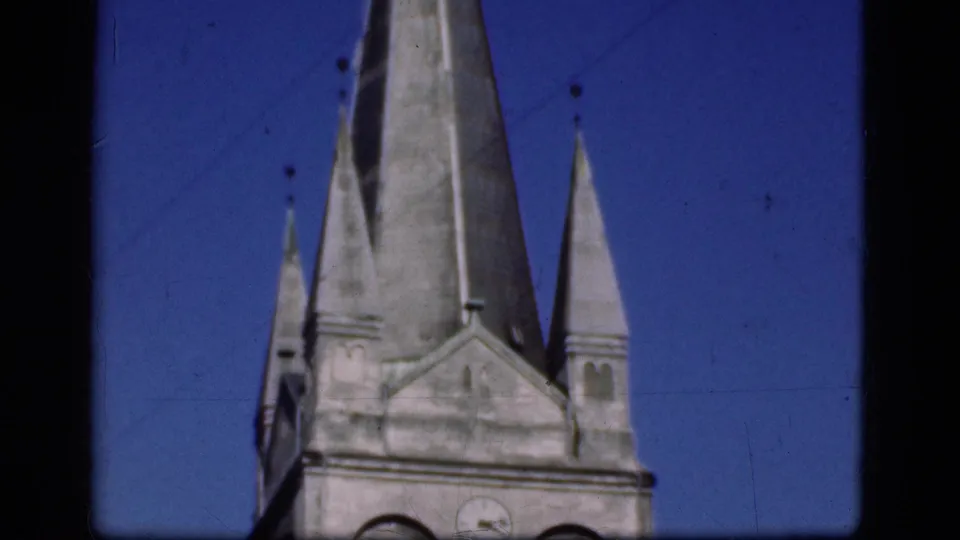 1975 Denmark 8mm frame focused on church spires, a gabled stone tower, roof edges, and open blue sky.