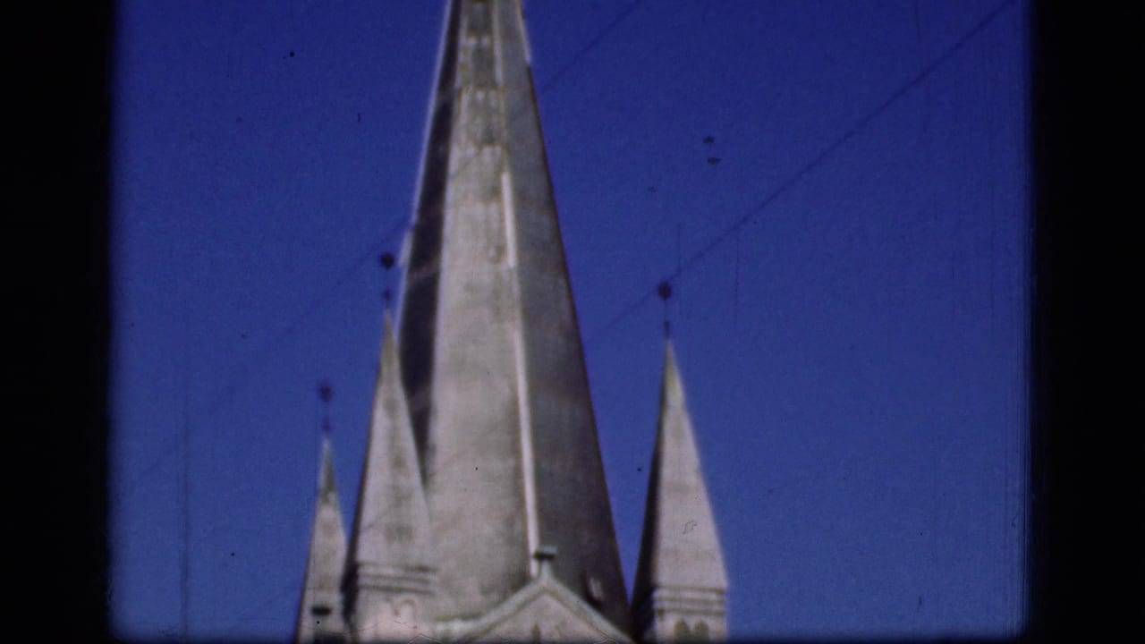 1975 Denmark 8mm frame showing tall pointed spires or stone roof forms against a blue sky, with dark film borders visible.