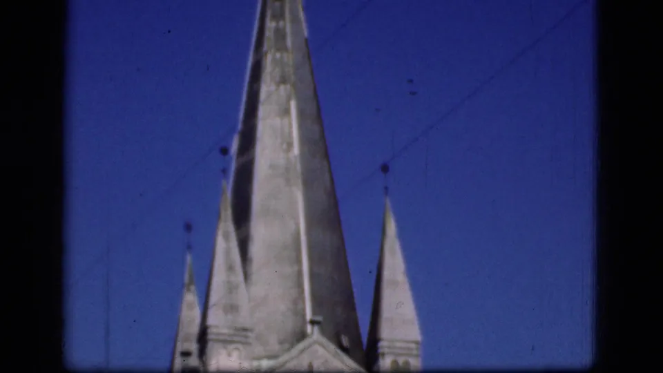 1975 Denmark 8mm frame showing tall pointed spires or stone roof forms against a blue sky, with dark film borders visible.