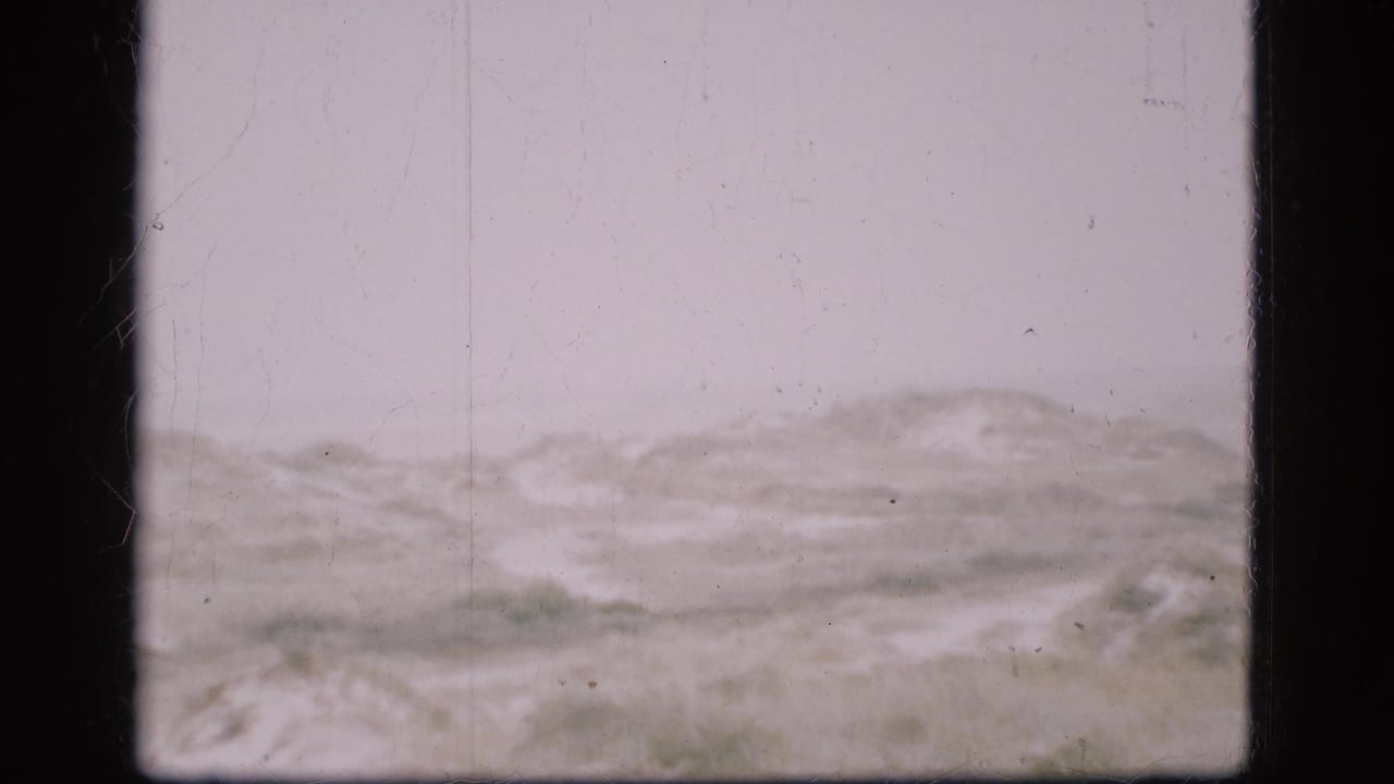 1975 Denmark 8mm frame showing a distant, low hilly or dune-like landscape under a pale sky, with visible film grain and edge borders.
