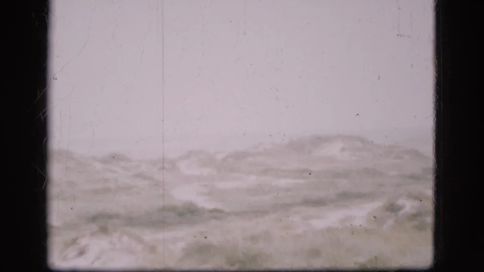 1975 Denmark 8mm frame showing a distant, low hilly or dune-like landscape under a pale sky, with visible film grain and edge borders.