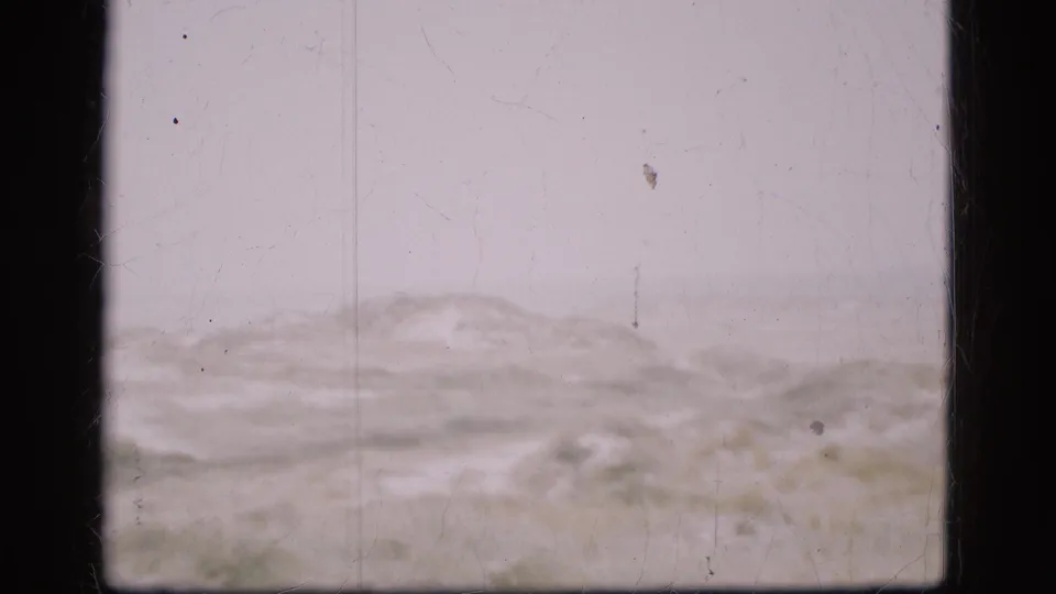 1975 Denmark 8mm frame with low dune-like ground near the lower edge, open pale sky, grain, and small film marks visible throughout.