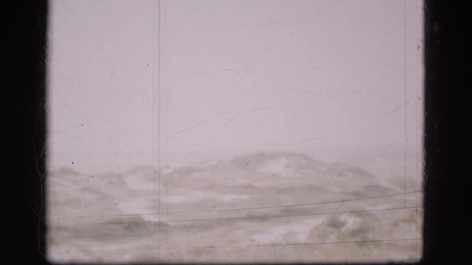 1975 Denmark 8mm frame showing an empty low landscape, likely dunes or hills, with washed exposure, dust specks, scratches, and dark frame edges.
