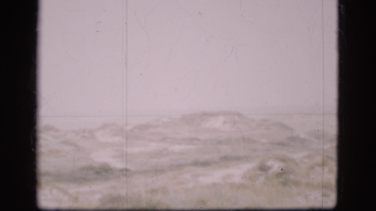 Pale cloudy sky above a low barren ridge or frozen field with dark 8mm frame borders.