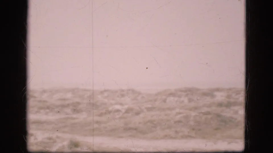 Static 8mm frame from Denmark showing a bleak, open landscape under a pale cloudy sky, with no identifiable people or property.