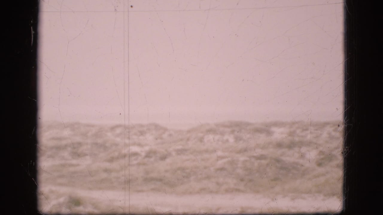 1975 Denmark 8mm frame showing pale overcast sky above low sandy dunes or scrubby terrain with visible film scratches and gate edges.