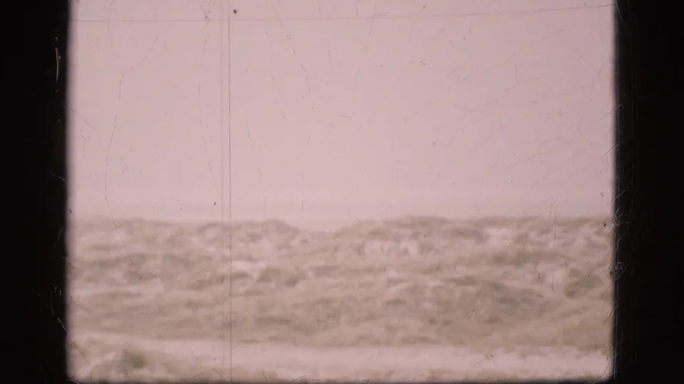 1975 Denmark 8mm frame showing pale overcast sky above low sandy dunes or scrubby terrain with visible film scratches and gate edges.