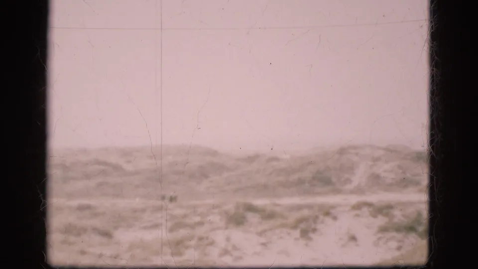 1975 Denmark 8mm view of low sandy dunes or scrubland with a faint track, pale sky, soft focus, and visible film grain and scratches.