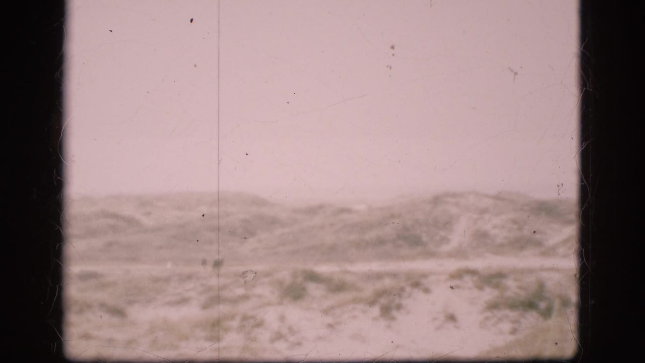 1975 Denmark 8mm frame showing snow-covered low hills or dunes under an overcast sky with visible film scratches and gate edges.