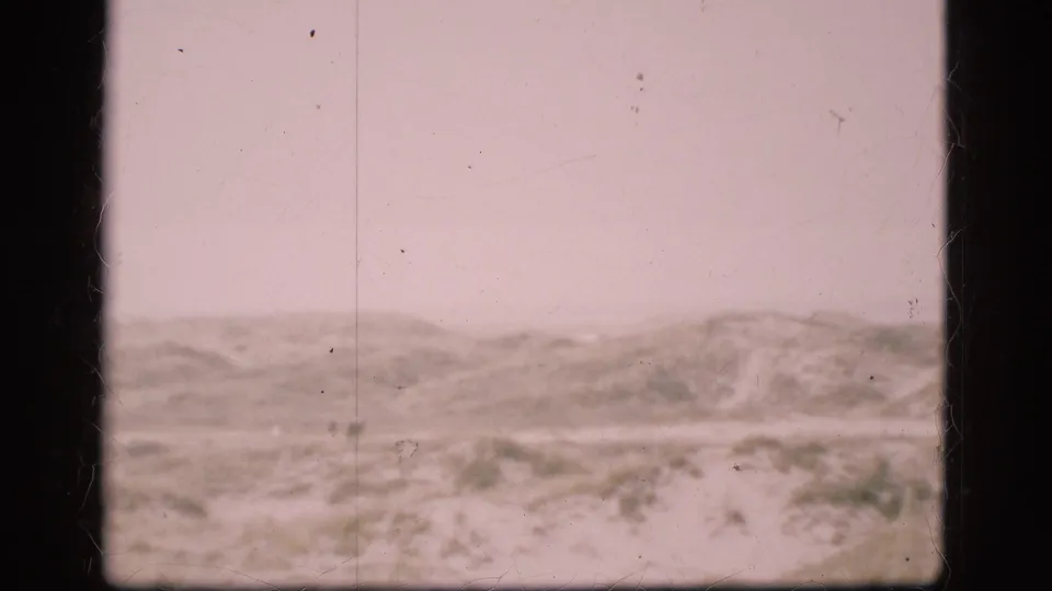 1975 Denmark 8mm frame showing snow-covered low hills or dunes under an overcast sky with visible film scratches and gate edges.