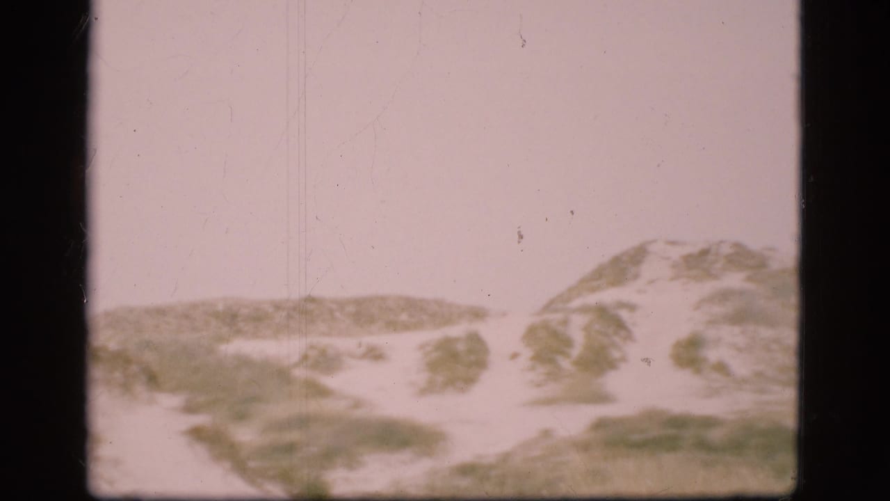 1975 Denmark 8mm frame showing low sand dunes with patchy grass and a pale washed sky.