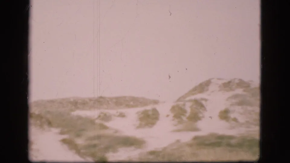 1975 Denmark 8mm frame showing low sand dunes with patchy grass and a pale washed sky.