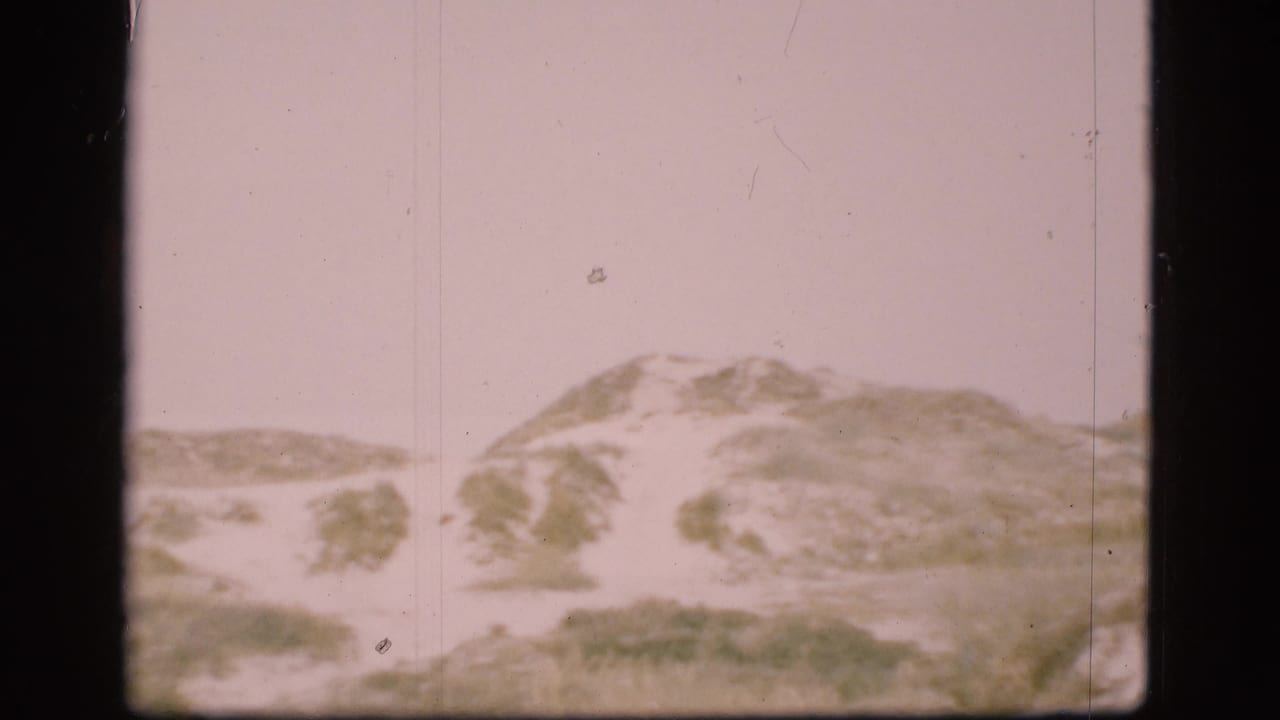 1975 Denmark home-movie frame of a dune ridge with muted grasses and soft 8mm exposure.